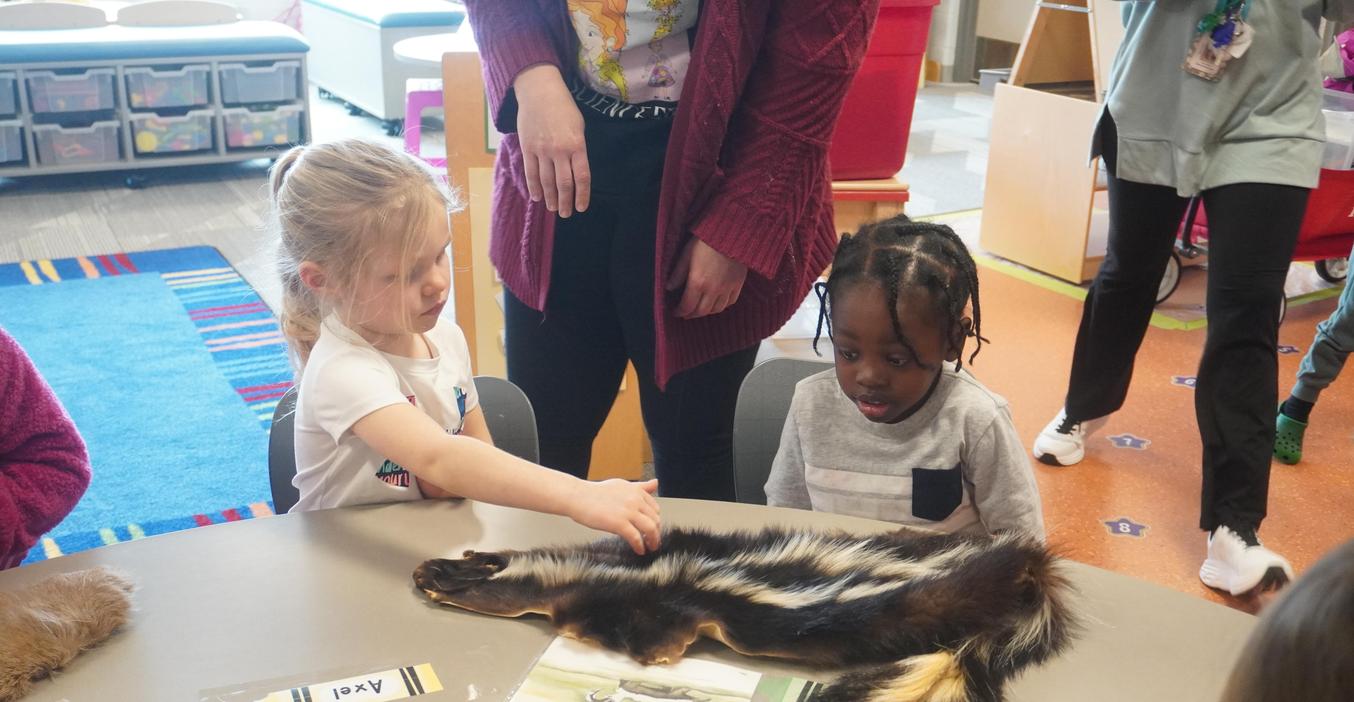 Two students feel a skunk pelt as they learn about how animals stay warm in winter.
