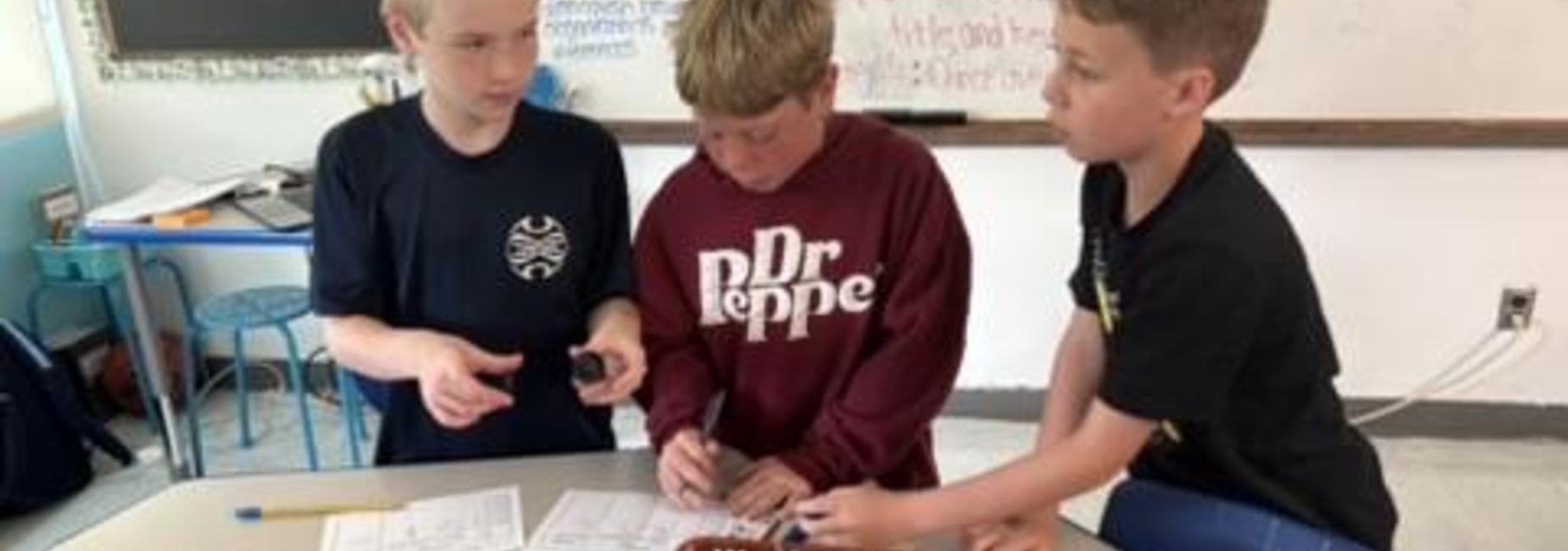 Three students collaborating on a project at a classroom table.