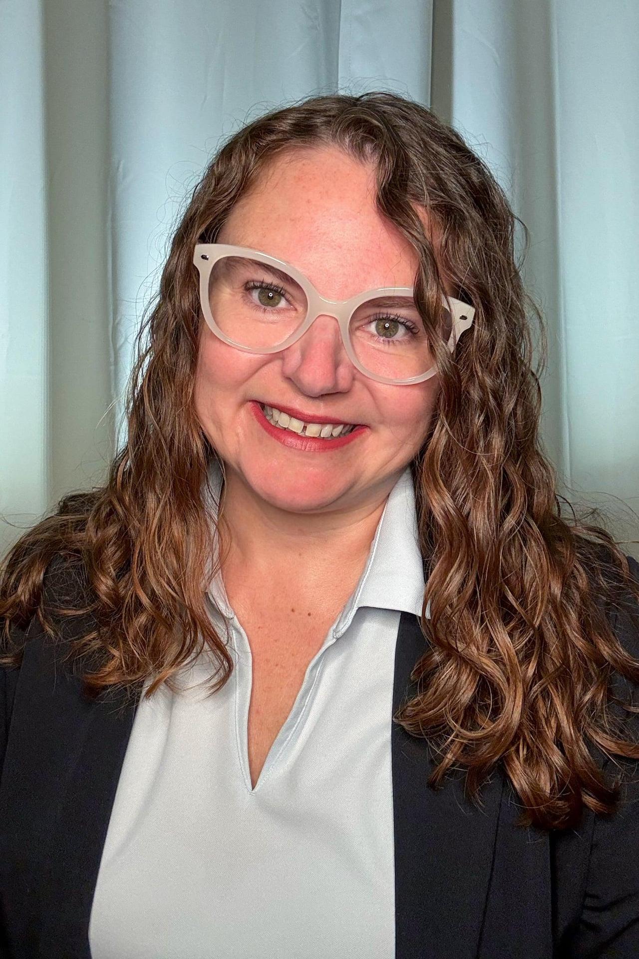 Girl with curly brown hair and glasses smiling