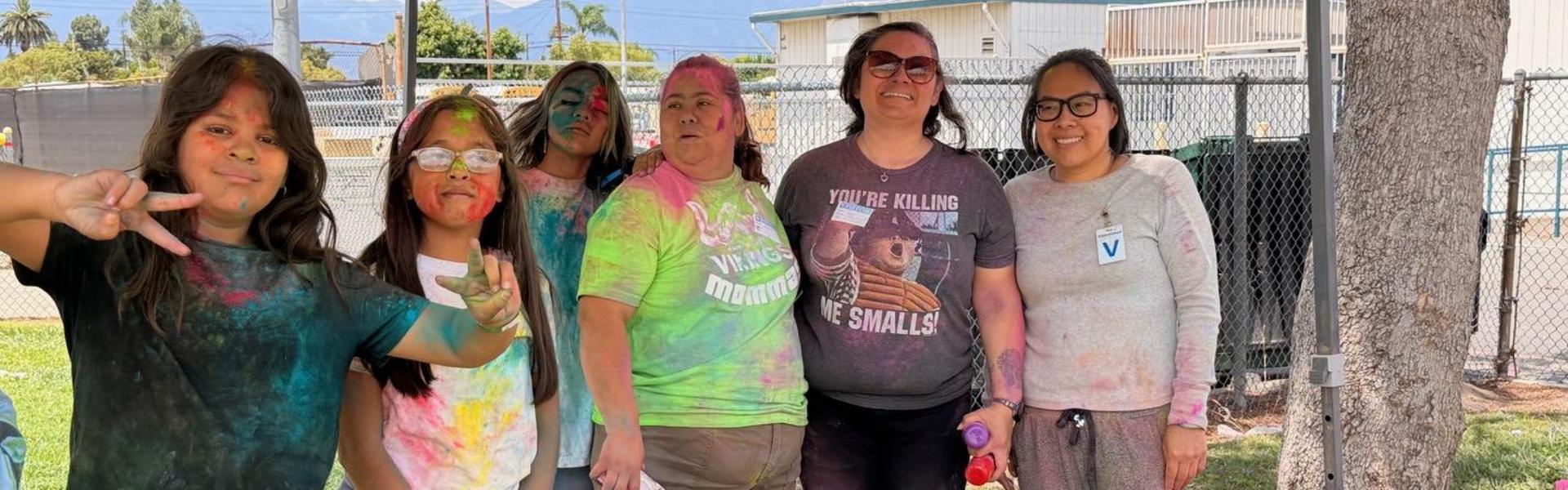 Group of five people, including children and adults, showing off colorful powder stains.