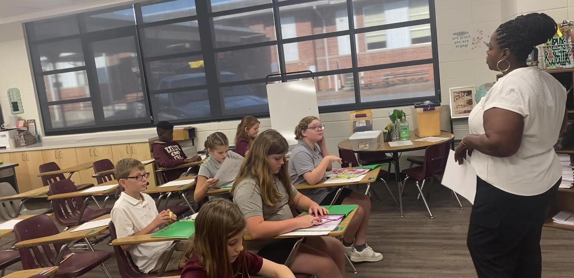 Students seated in a classroom attentively listening to a teacher.