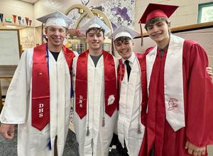 Four graduates stand together in a hallway