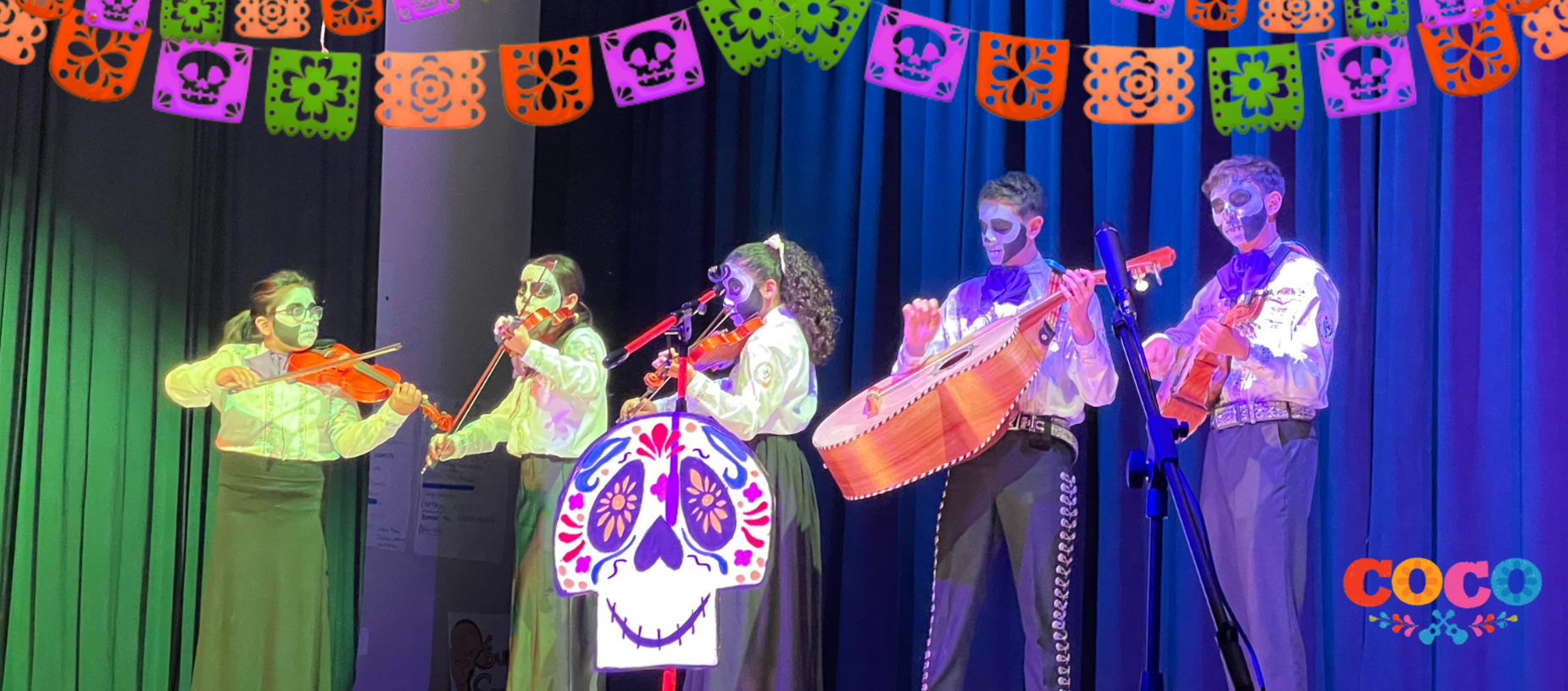 Performers in traditional attire with face paint on stage playing musical instruments.