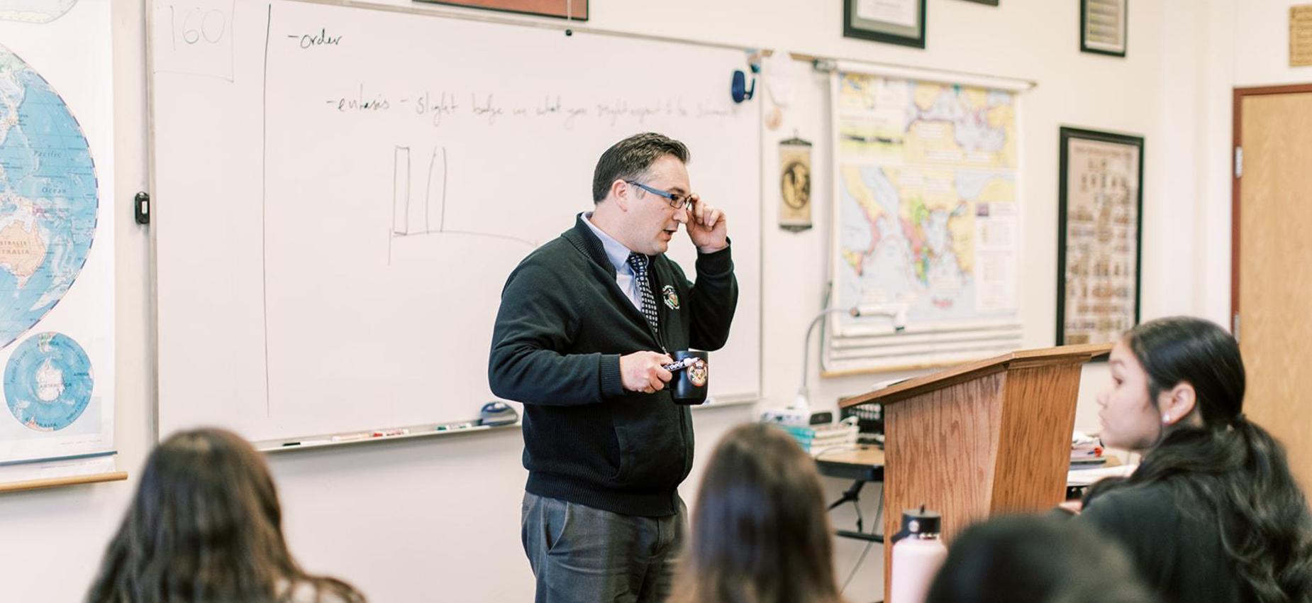 Teacher leads a lesson at the whiteboard beside a globe and maps