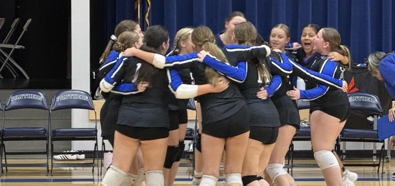 A group of volleyball players celebrating in a huddle on the court.