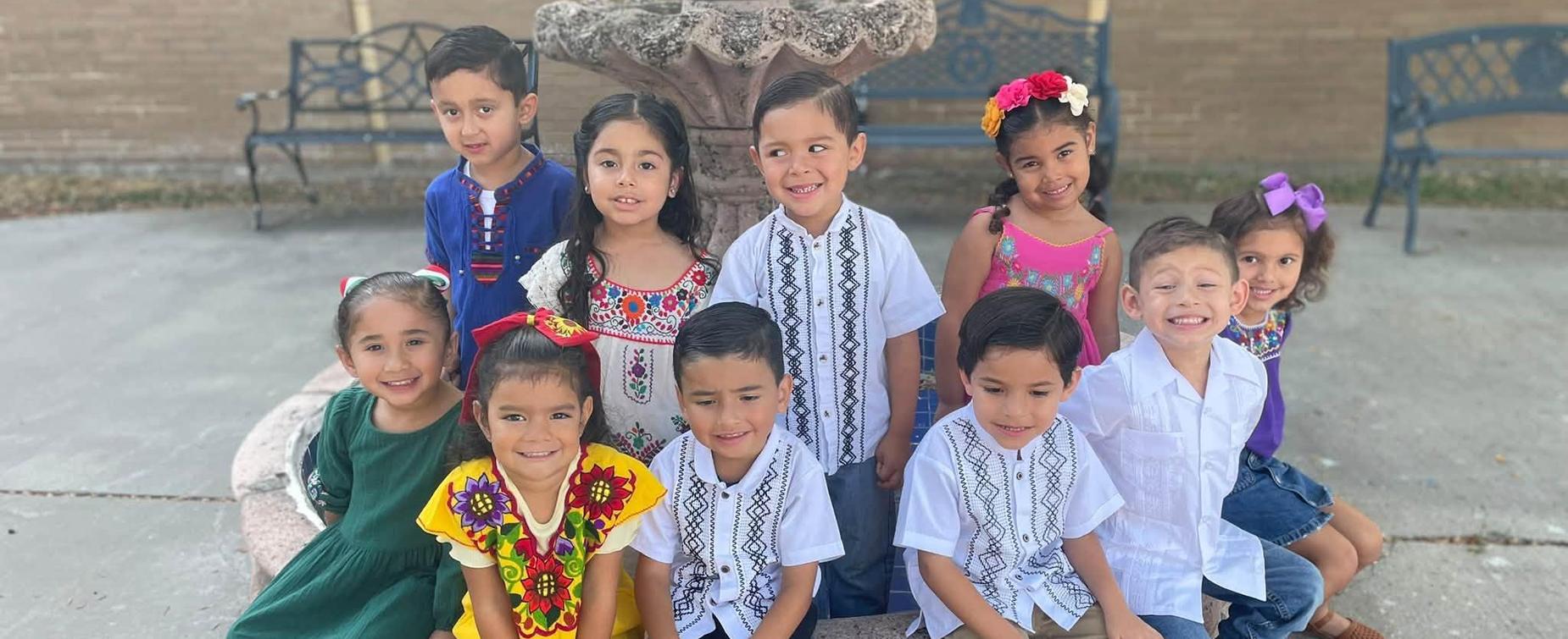 Group of children in colorful traditional clothing posing together outdoors.