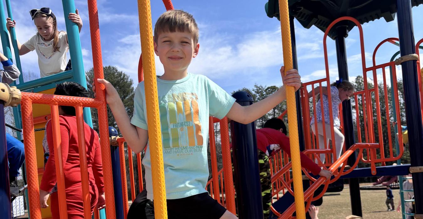 A boy posing on a climbing structure while others play in the background.