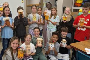 A group of children showing off their decorated bottles in a classroom.
