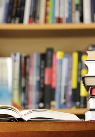 Open book in foreground with stacked books and blurred library shelf in background.