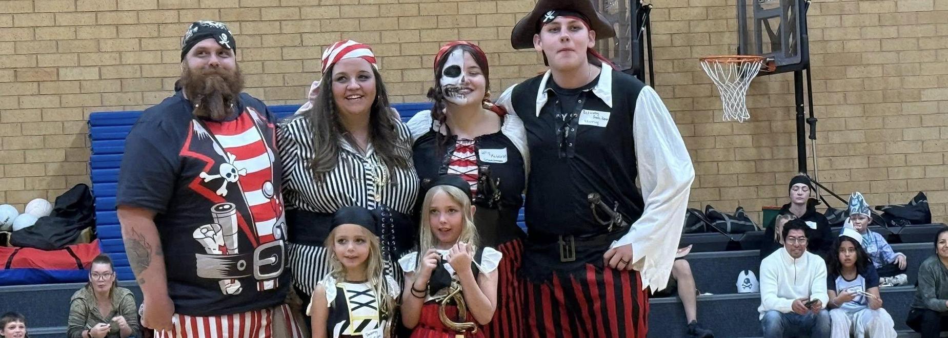 A group of six people dressed in pirate costumes, standing together in a gymnasium.