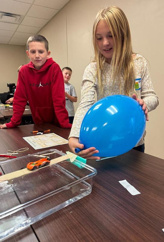 Girl releasing a balloon while a boy observes at a science table.