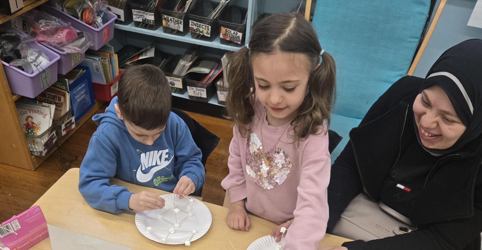 Children and adult building a structure with materials at a table.