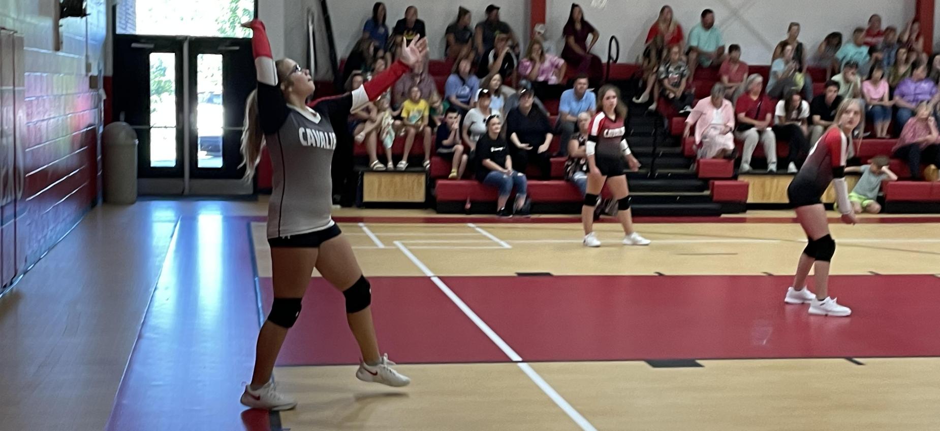 A volleyball player serves the ball while two players watch.
