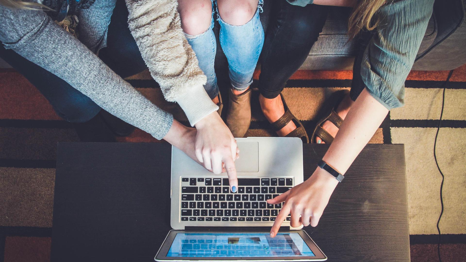 Three people pointing at a laptop screen together.