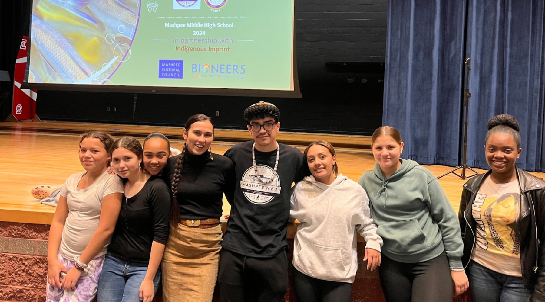 A group of students stands together in front of a presentation screen.