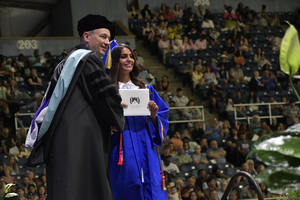 Student and superintendent smiling and holding diploma on stage