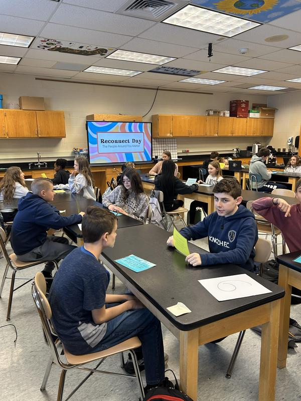 room full of students sitting across the table from each other holding cards