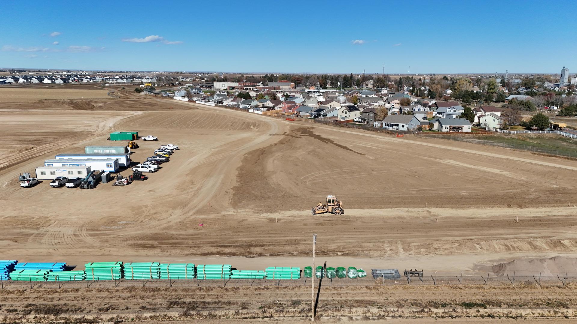 Aerial view of a cleared construction site with vehicles and a nearby neighborhood.