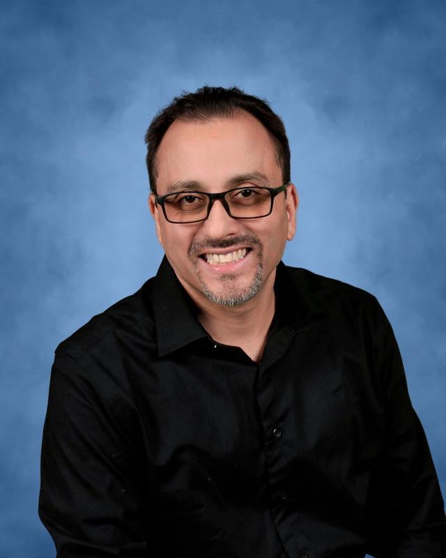 Smiling man in a black shirt against a blue background.