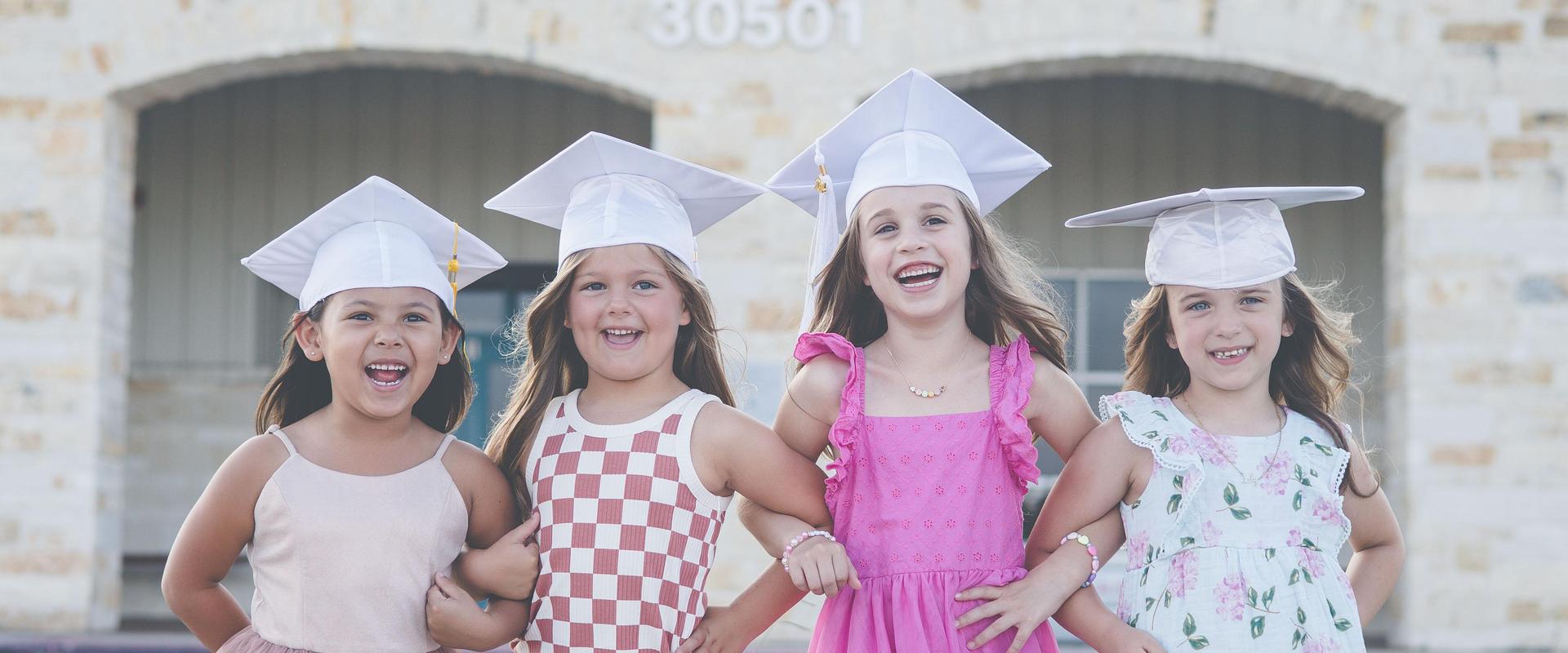 Four smiling girls in graduation caps standing side by side, celebrating together.