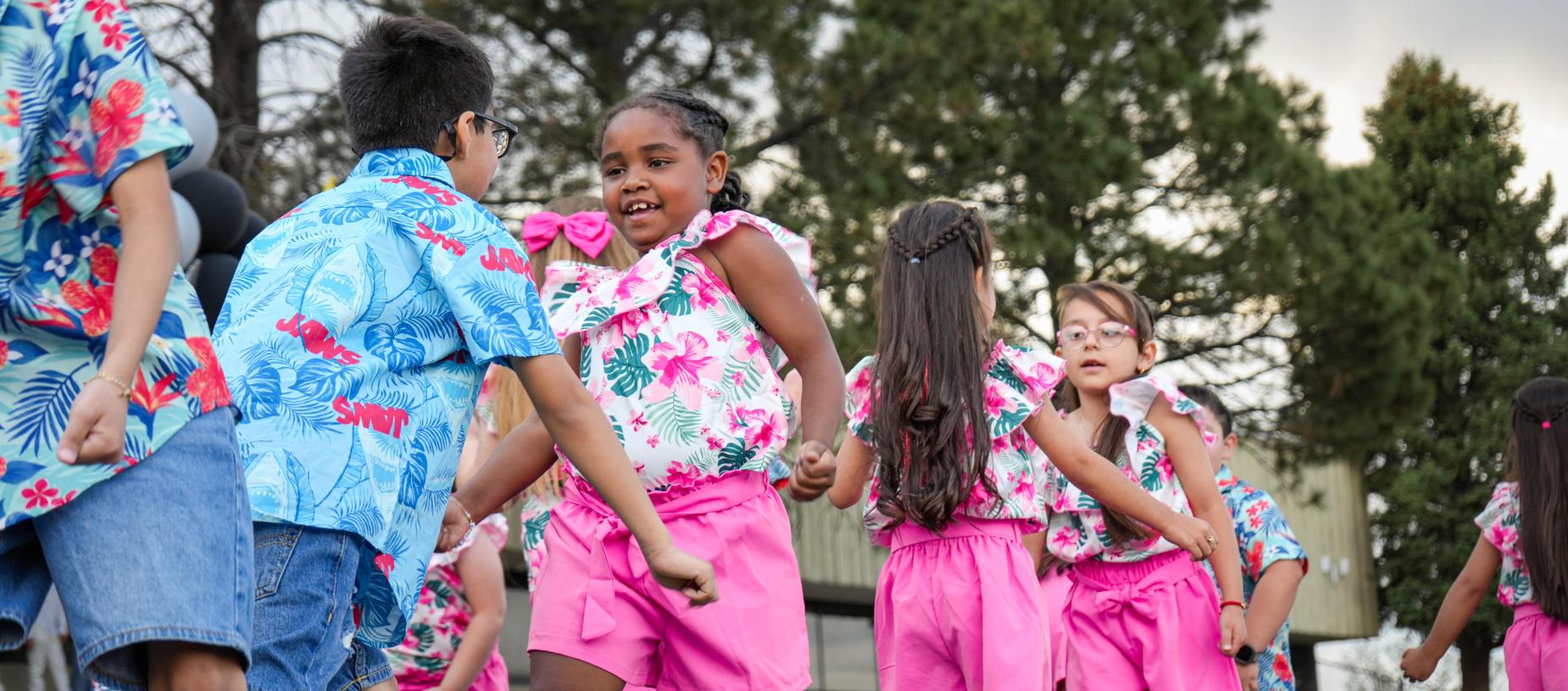 Children dancing in colorful floral outfits outdoors.