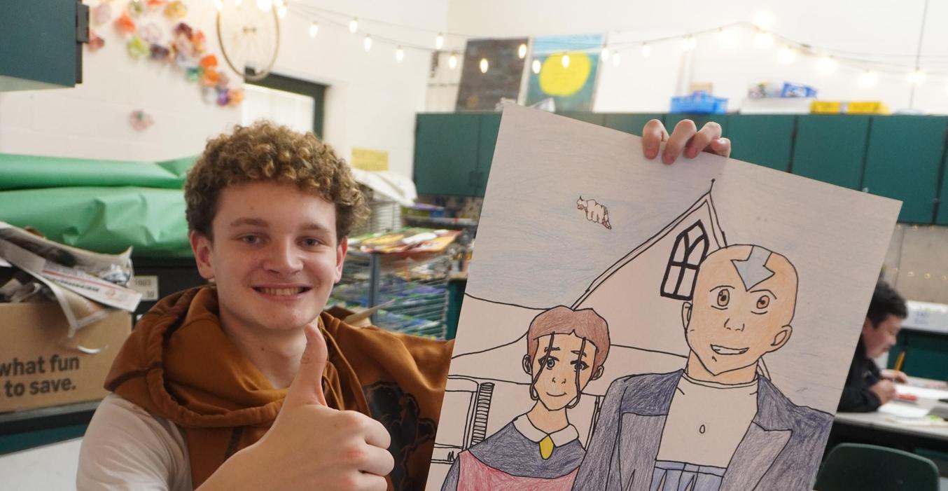 A student gives a thumbs up while showing his artwork.