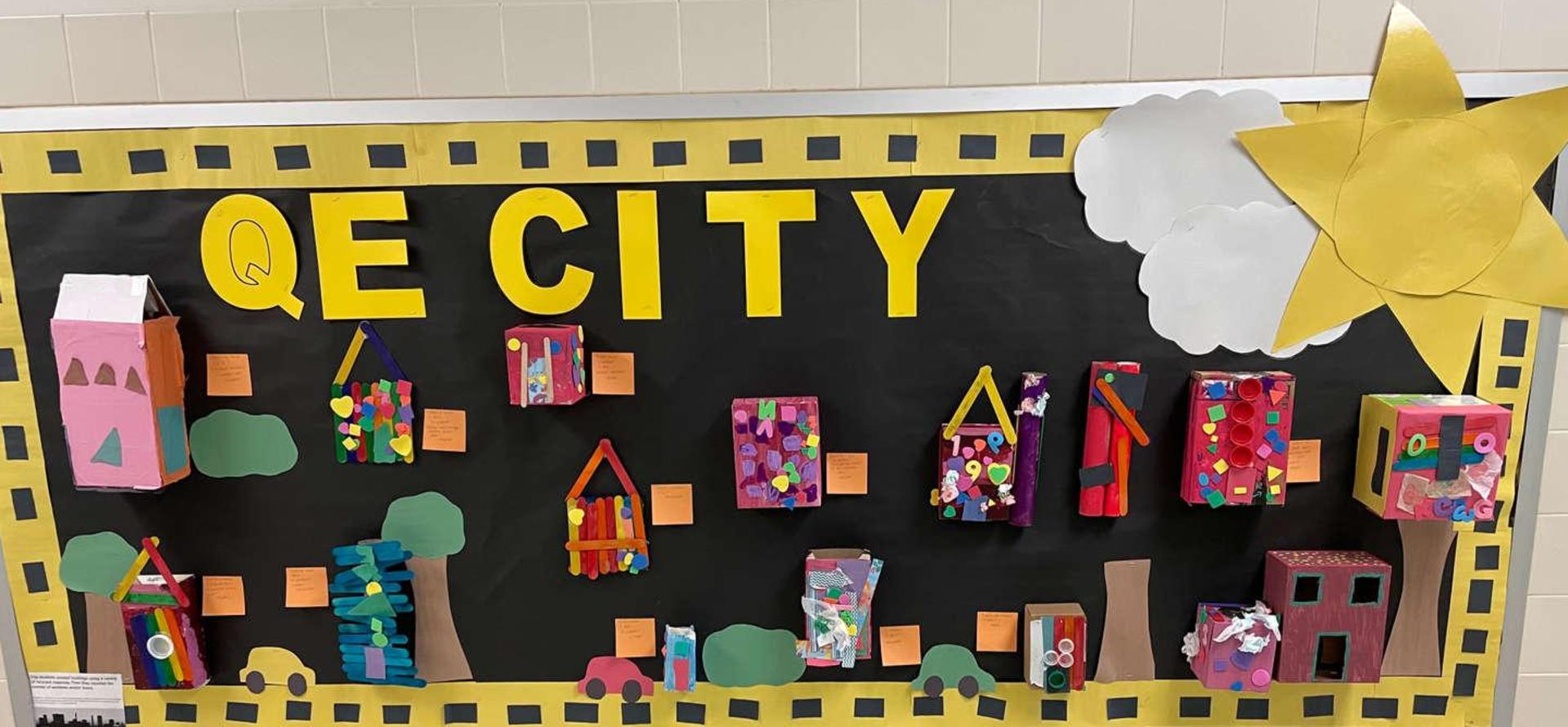 Colorful art display of 3D houses and trees on a blackboard.