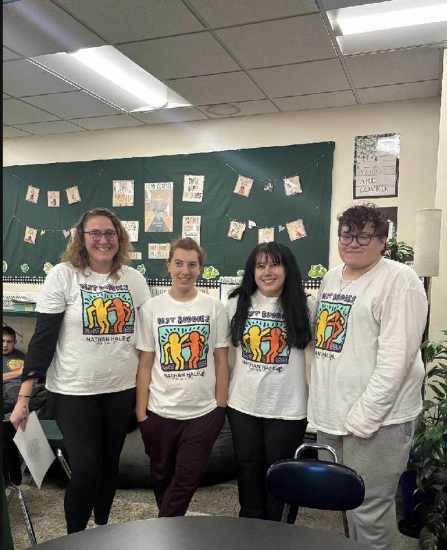 A group of four students wearing matching t-shirts posing together in a classroom.