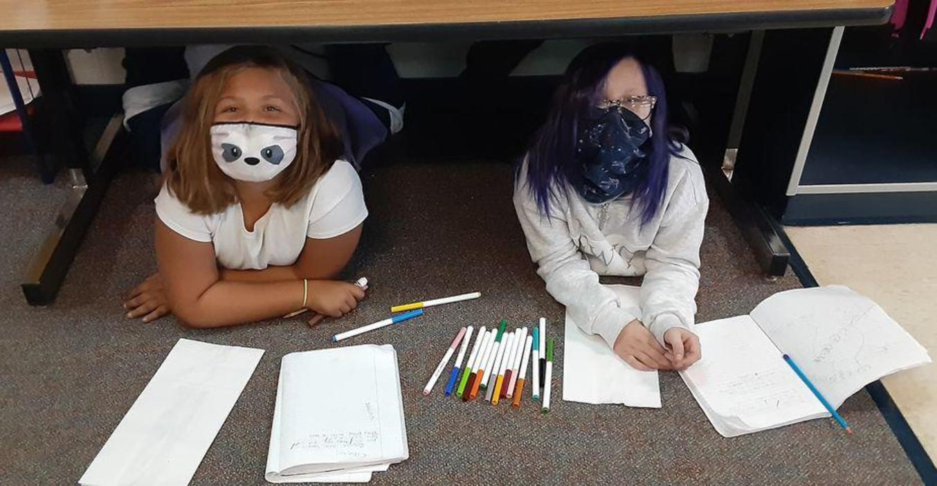 Two girls work on decorating bags for Kids Food Basket.