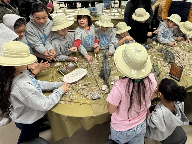Group of children wearing hats engaged in an educational activity at a decorated table.