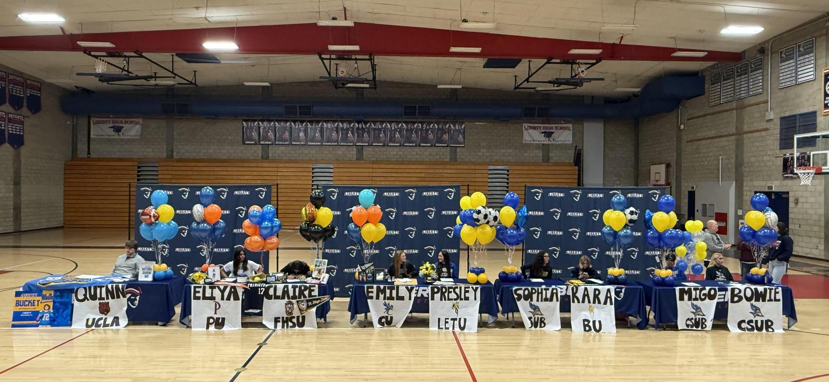 A celebration event with balloons and tables displaying names of students committing to colleges.