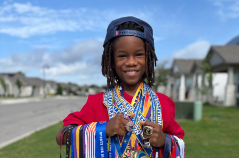 Ezra stands with multiple medals won in sporting competitions