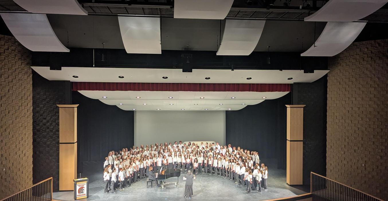 A large choir performing on stage in a theater with a dark backdrop.