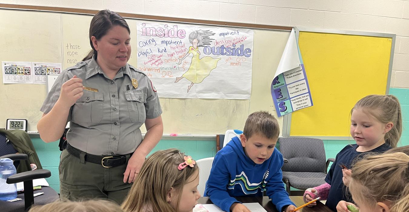 A ranger leading a group of children in an educational activity at a classroom table.