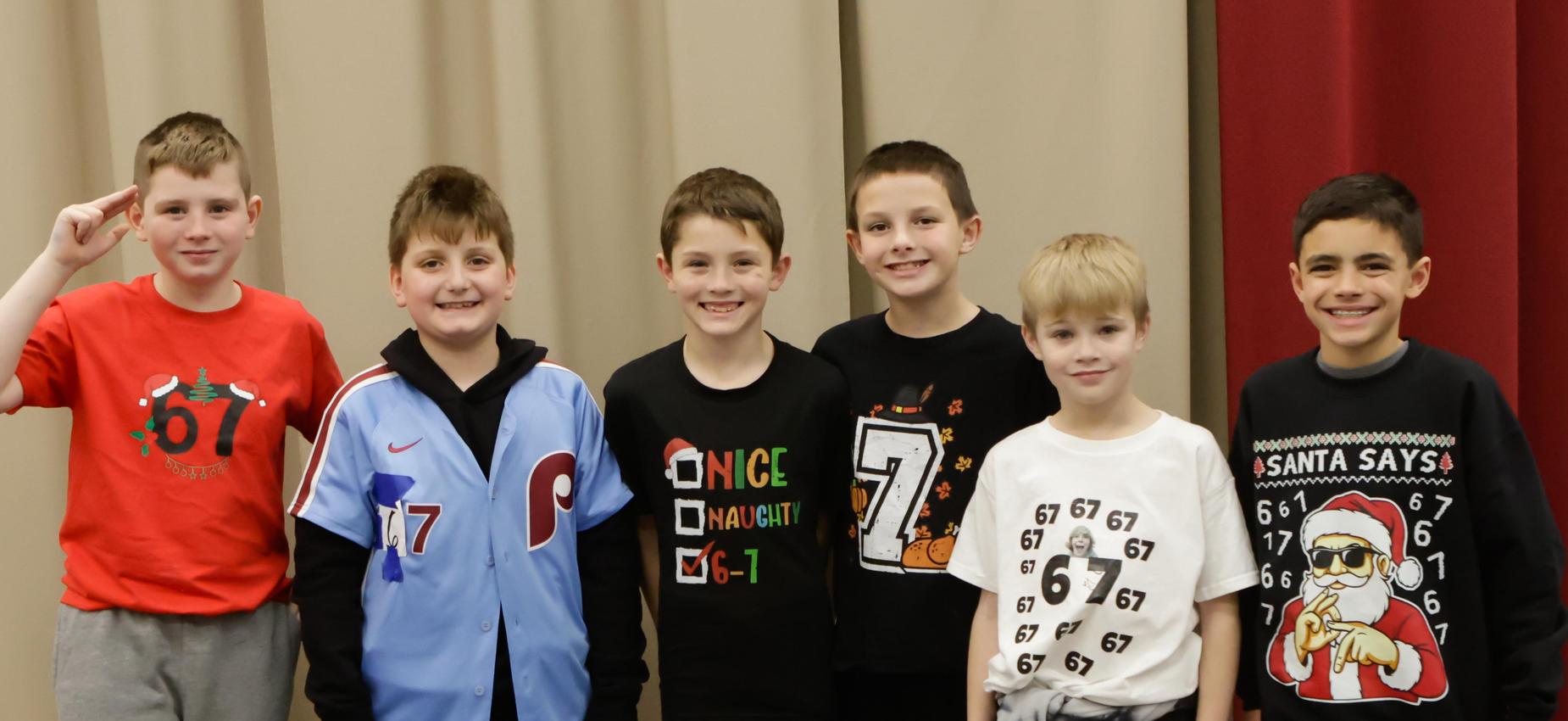 Six boys standing in a row, wearing various shirts with numbers and designs.