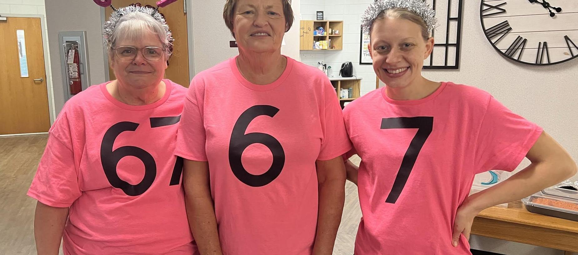 Three women in matching pink shirts with large black numbers, smiling together.