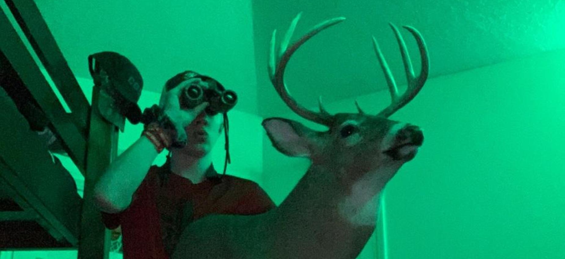 A student holds binoculars and a deer.