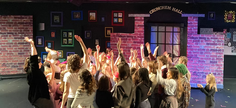 Young cast members on stage sharing a celebratory moment.