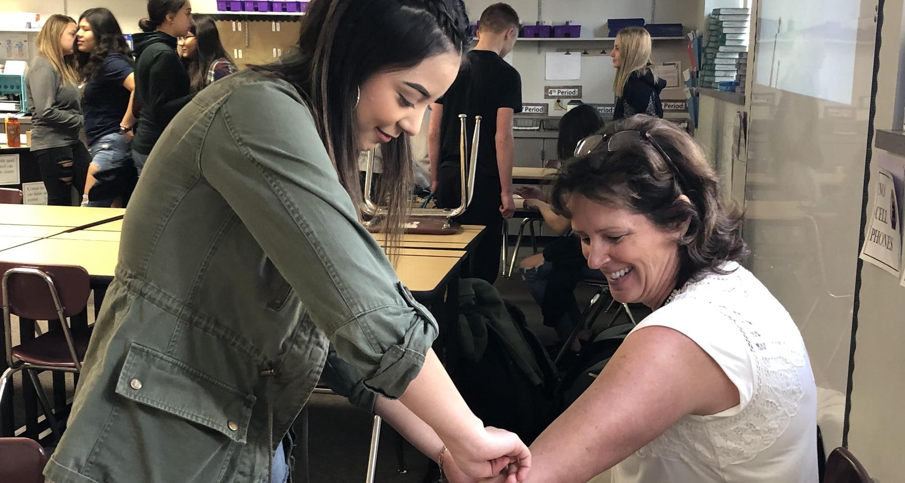 Female students checking teacher's blood pressure.