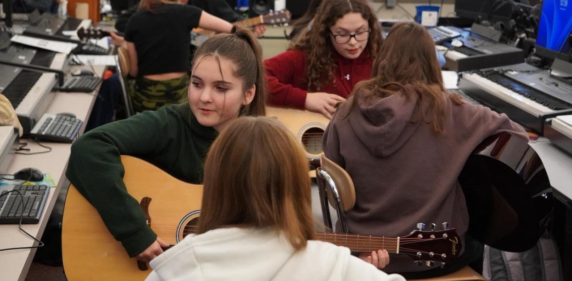 four girl students hold guitars while learning in computer lab