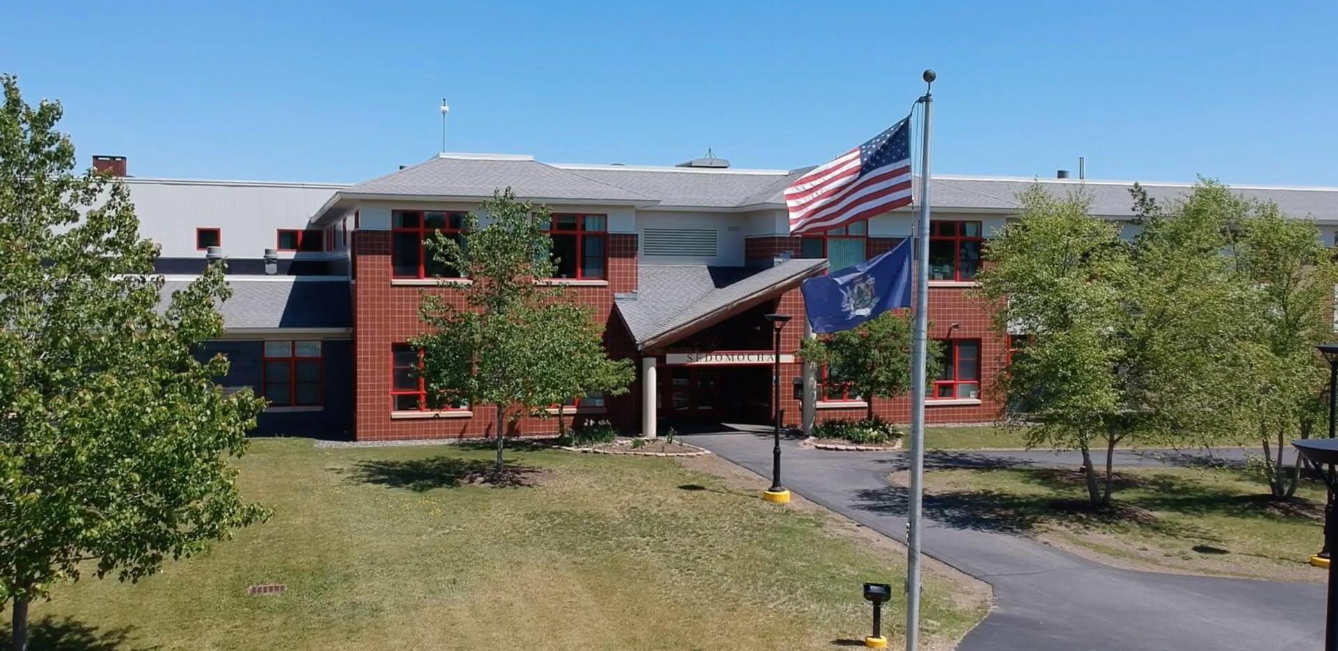 Exterior view of a school building with trees and an American flag.