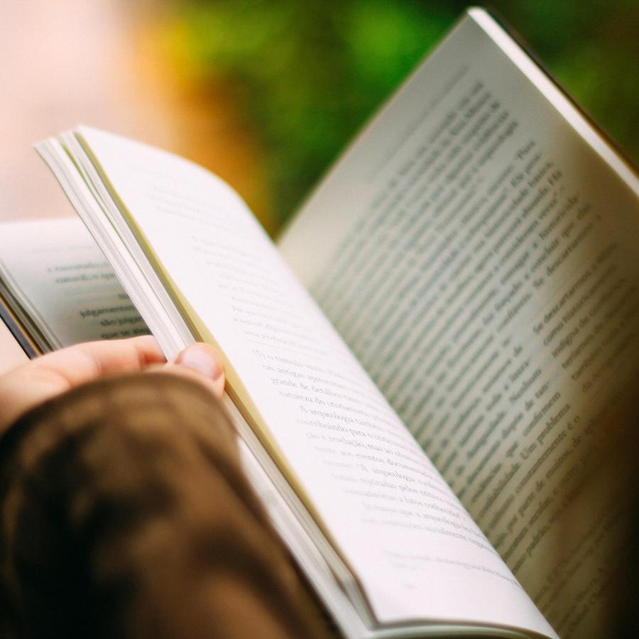 A person holding an open book with visible text pages.