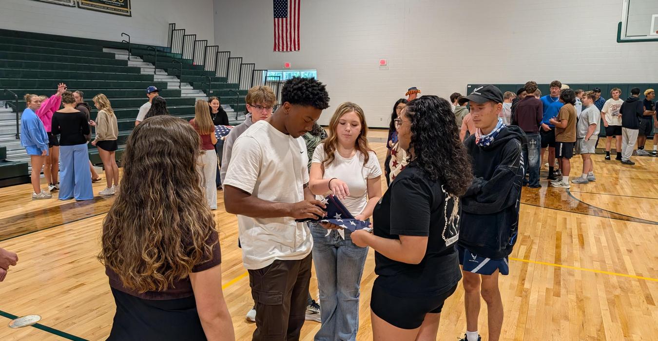 Students gather to work with flags while interacting in a gym setting.
