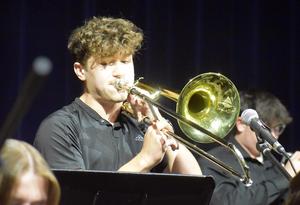 A young man plays the trombone while performing with a band.