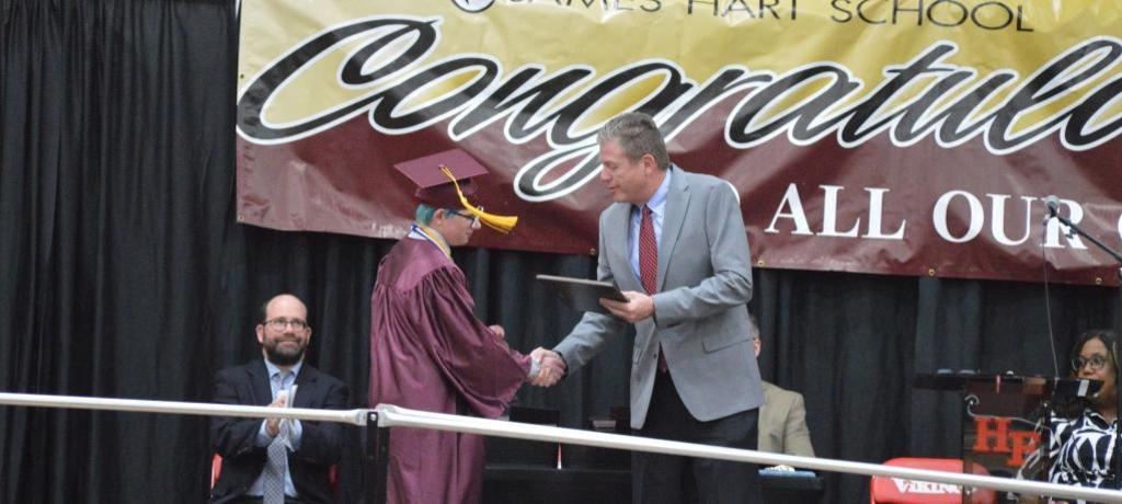 school board president shakes boy's hand while handing him an award