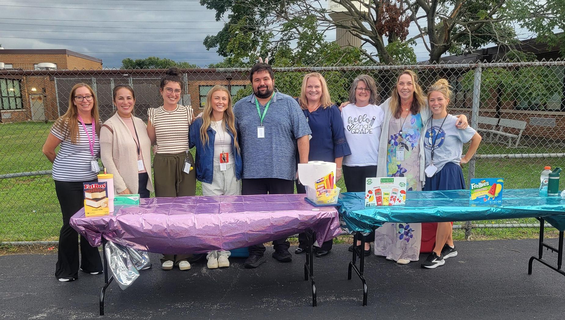 Group of people posing at tables with various items outdoors.