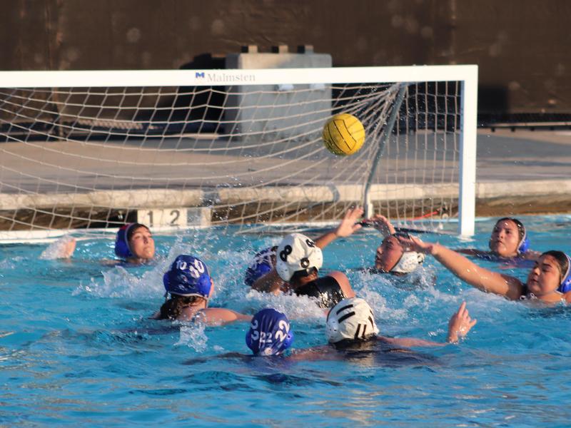 Water polo players competing near the goal in a pool.