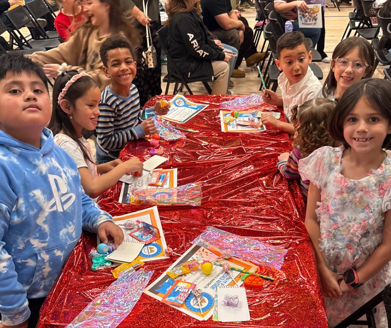 2nd grade students gathered around a red table-clothed table with books
