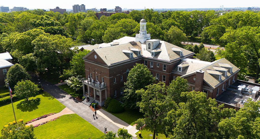 Aerial view of a historic brick building surrounded by lush green trees and lawns.