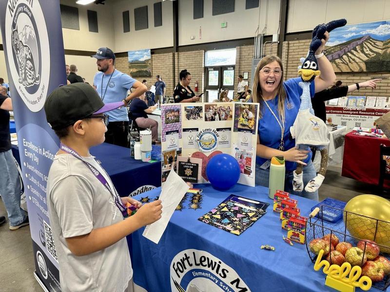 A student visits a school resource booth while a staff member holds up a roadrunner mascot plushie and smiles.